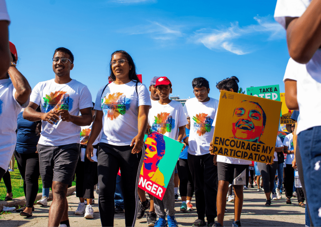 This image shows a large group of people walking outside in the sun. The crowd is walking as part of SAAAC's annual walk-a-thon.