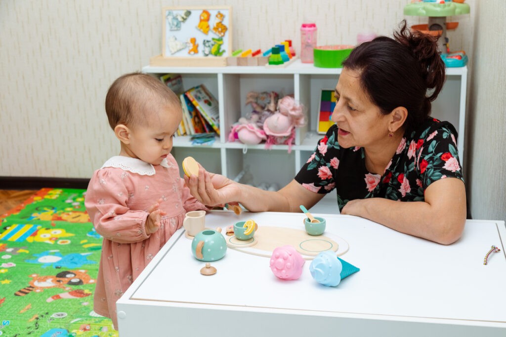 Grandmother and toddler playing with toys at home. Drinking tea from toy teapot