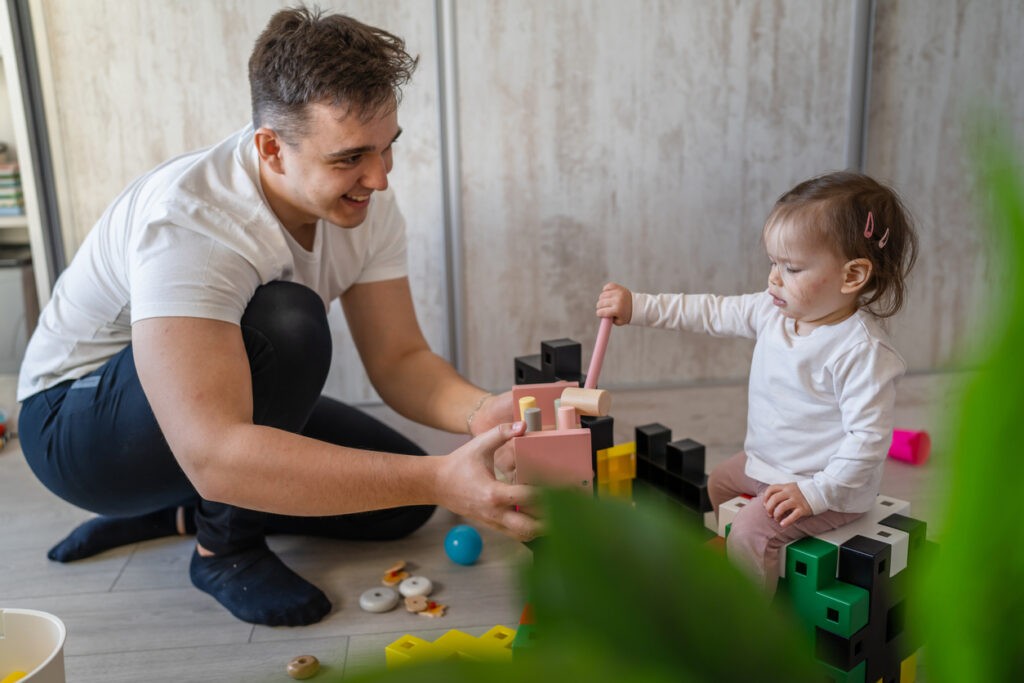 baby girl and her father young man with daughter playing at home happy sitting on the floor with toys