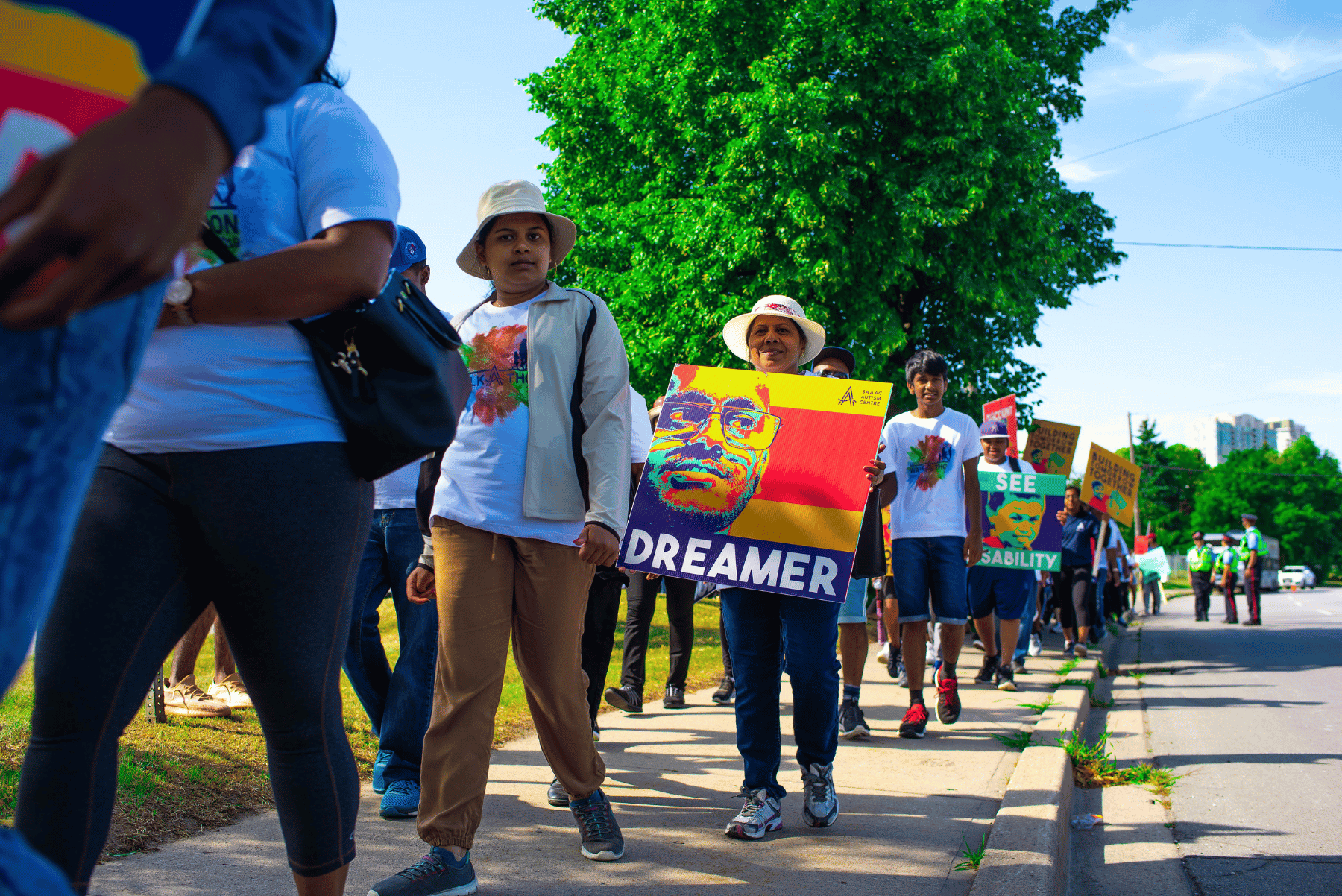 people walking towards camera during the walk-a-thon event. a lady with hat is holding a sign that reads "dreamer"