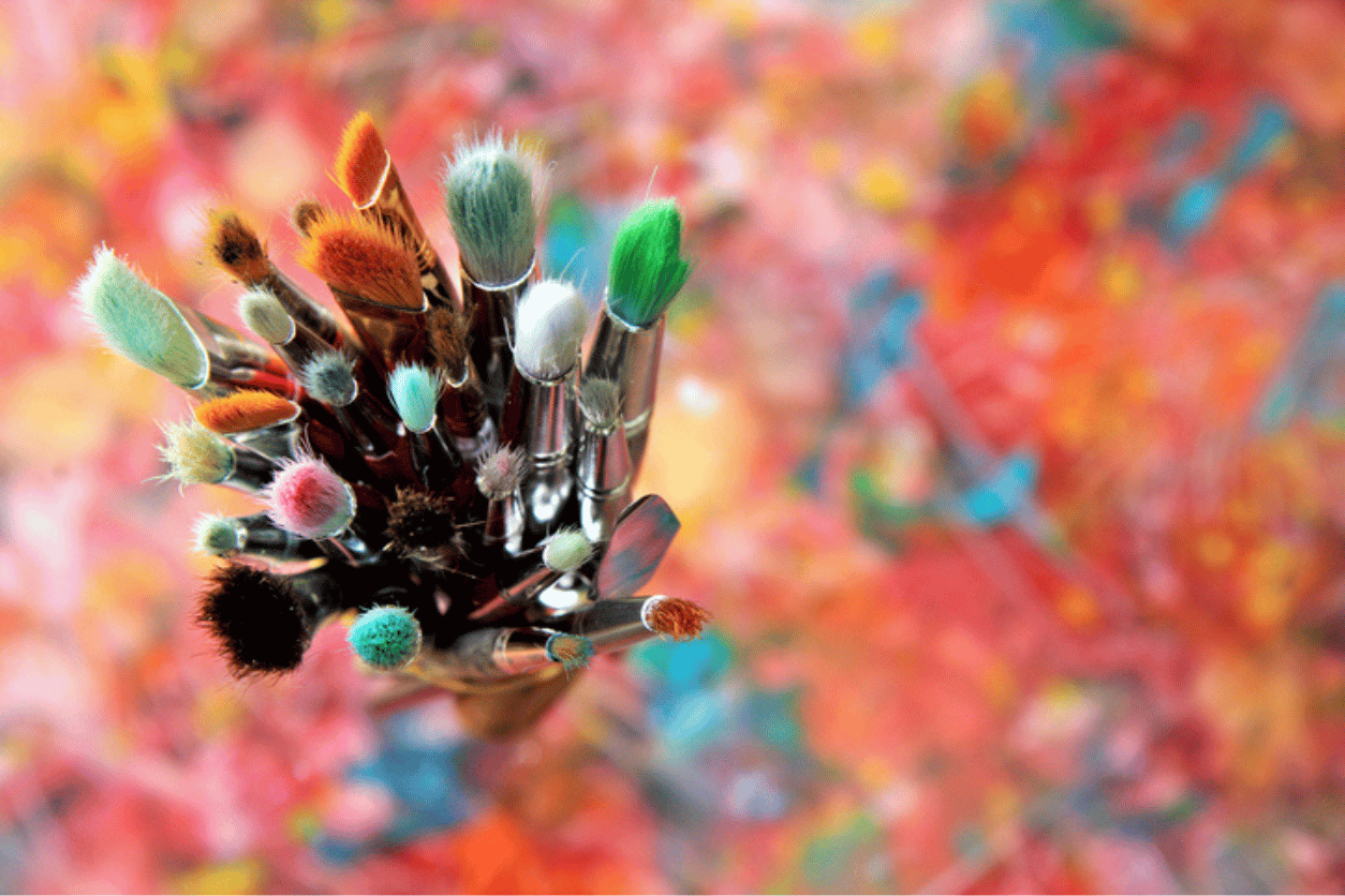Focus on a collection of paint brushes on top of a colourfully painting canvas
