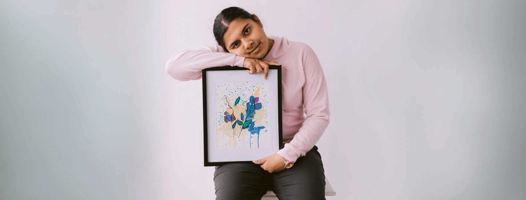 Taniya Moses holding her painting, which is framed