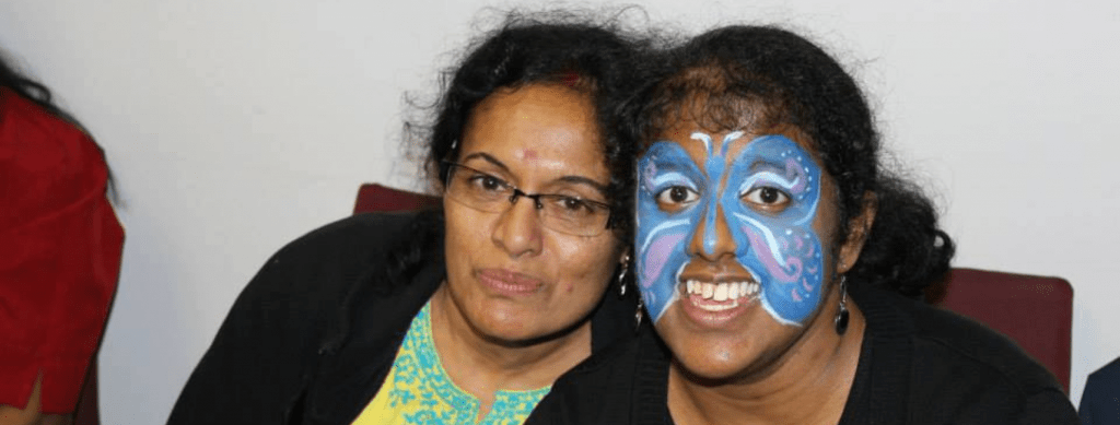 Smiling mother and daughter sitting together, with the daughter featuring vibrant butterfly face paint, showcasing their joyful bond.