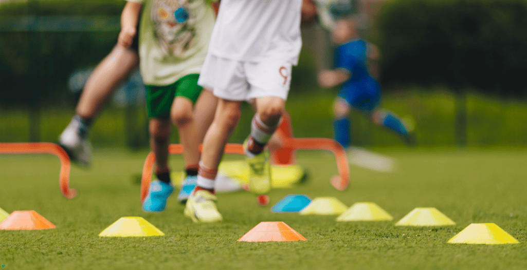 Children participating in a fun and active sports drill on a grass field, navigating colorful cones and hurdles to enhance coordination and agility.