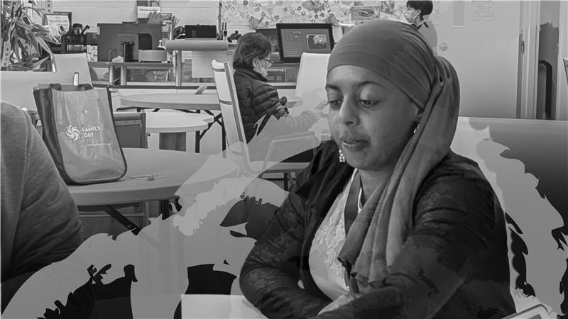 A woman wearing a headscarf sits at a table with her arms folded, looking down thoughtfully. She is in a community space with tables, chairs, and other people in the background. The image includes a semi-transparent graphic overlay of silhouettes. The photo accompanies a story about a SAAAC client who found employment in the community.