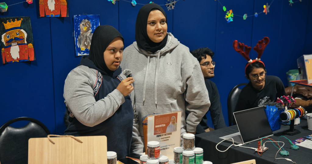 Vendor from Habibi Tea speaking with visitors at the 2025 SAAAC Holiday Market, showcasing products at their booth.
